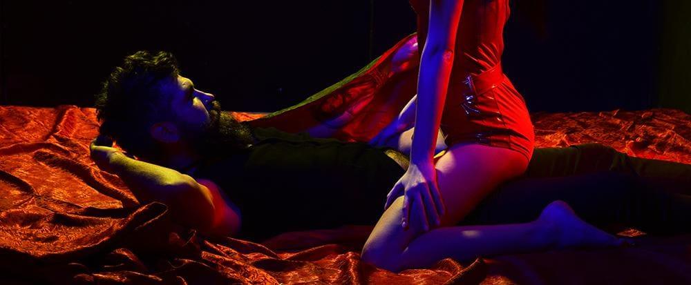 Couple in intimate pose on red satin sheets with dramatic red and blue lighting