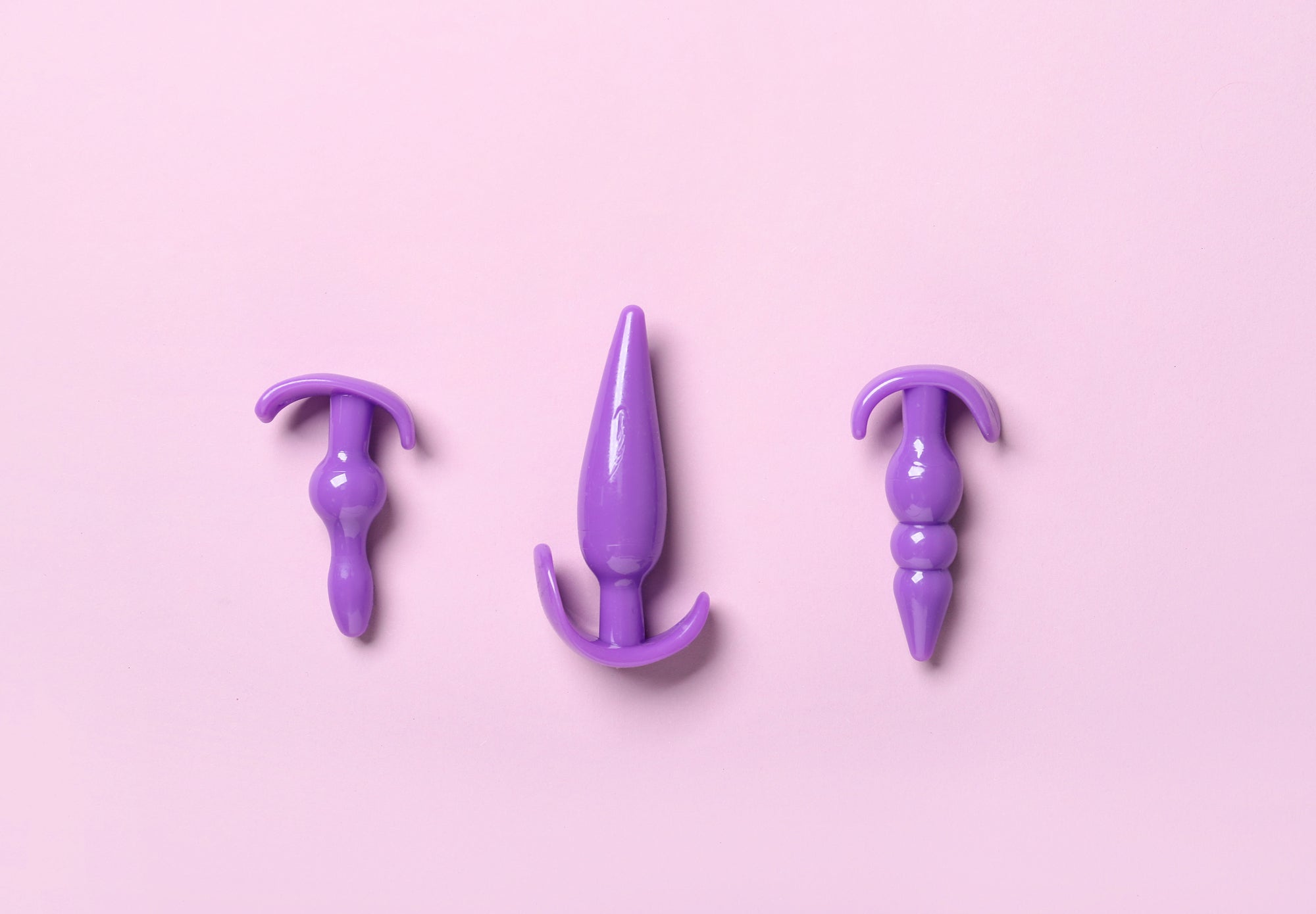 Three purple silicone butt plugs of different sizes on a light pink background.