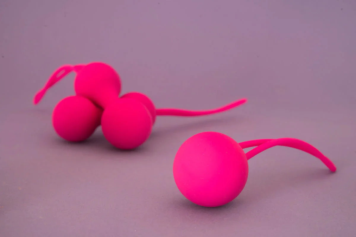 Two bright pink silicone adult pleasure toys on a neutral grey background
