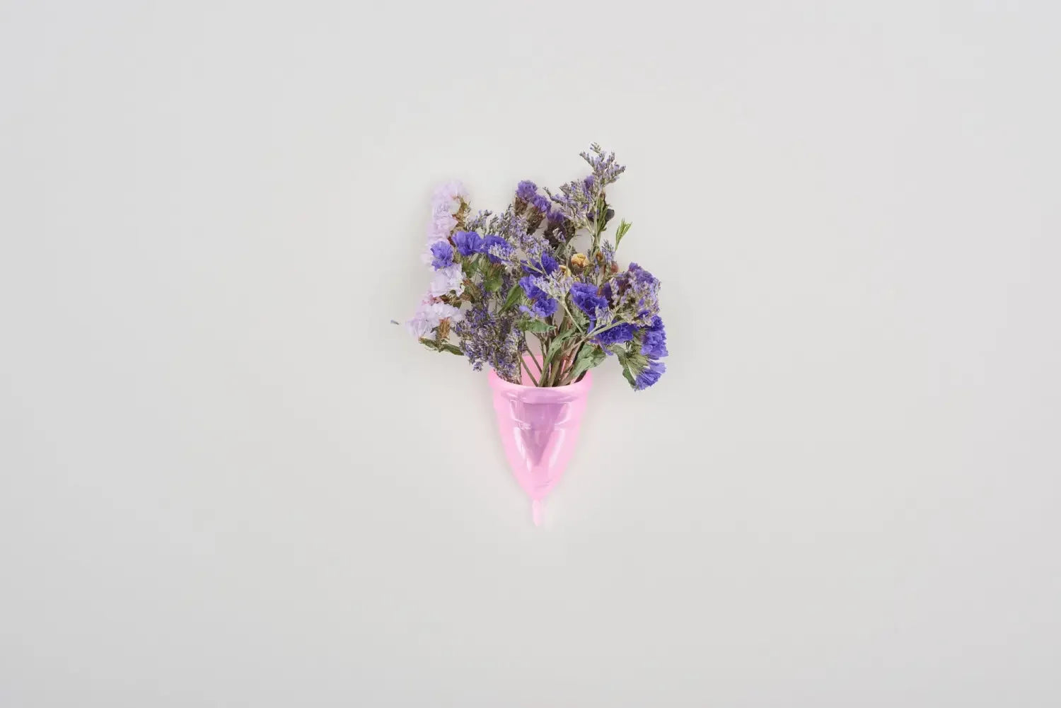 Small bouquet of purple and blue dried flowers held in a pink menstrual cup against a white background.