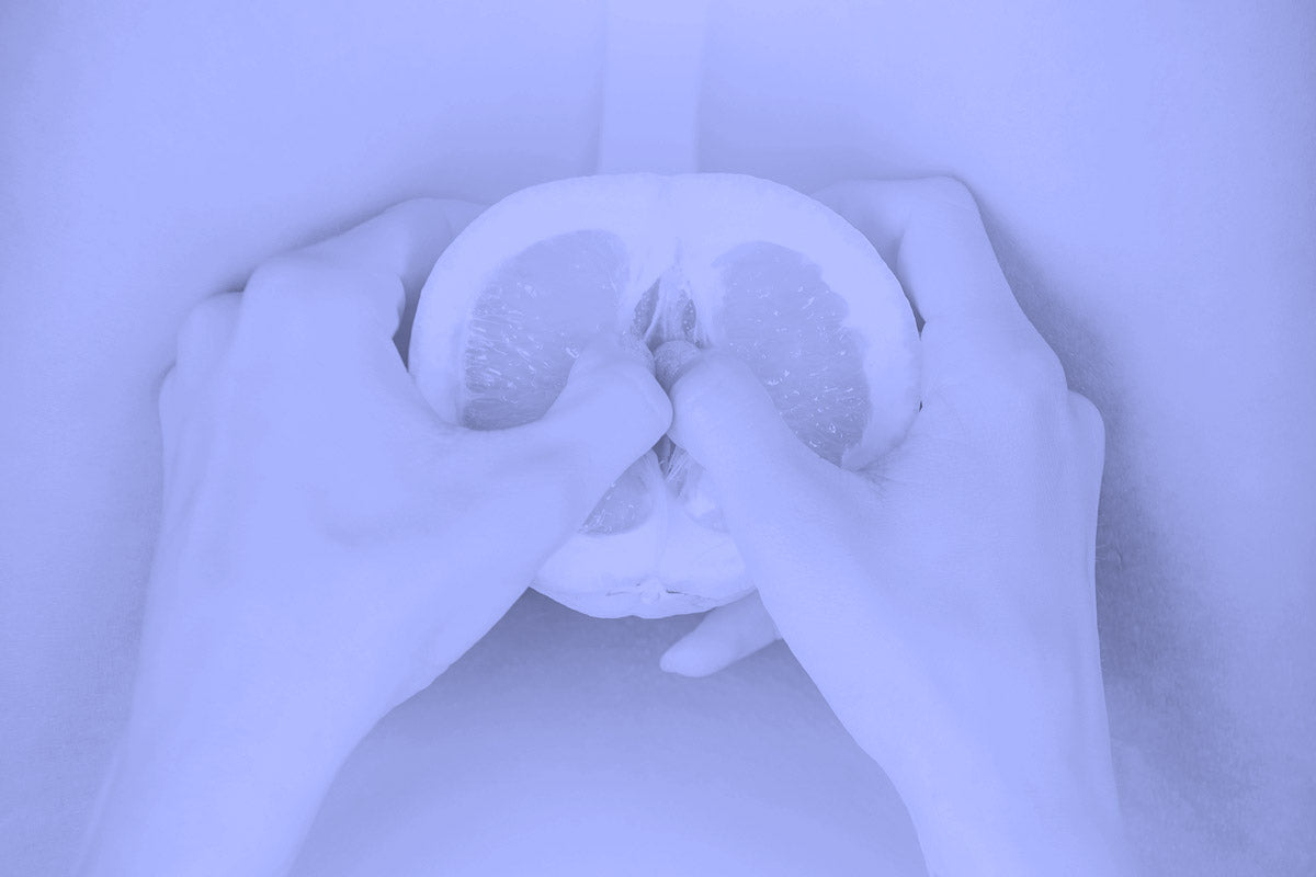 Hands holding and squeezing a sliced grapefruit against a purple backdrop.