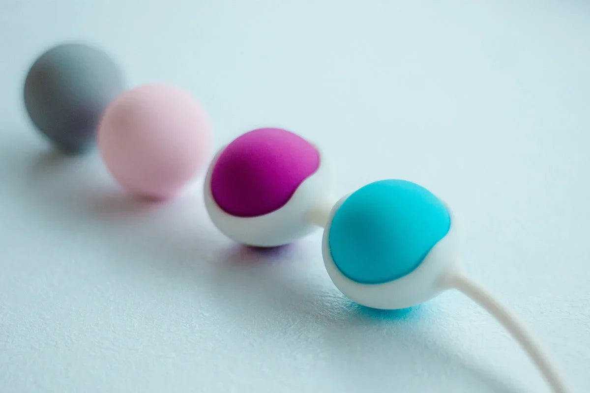 Four colorful silicone pelvic floor trainer balls in grey, pink, purple, and blue.