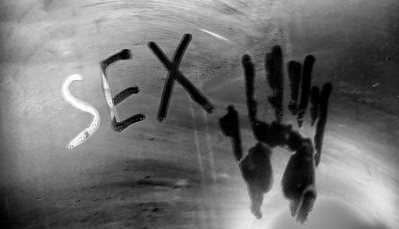 The word 'SEX' and a handprint written in condensation on a foggy glass surface.