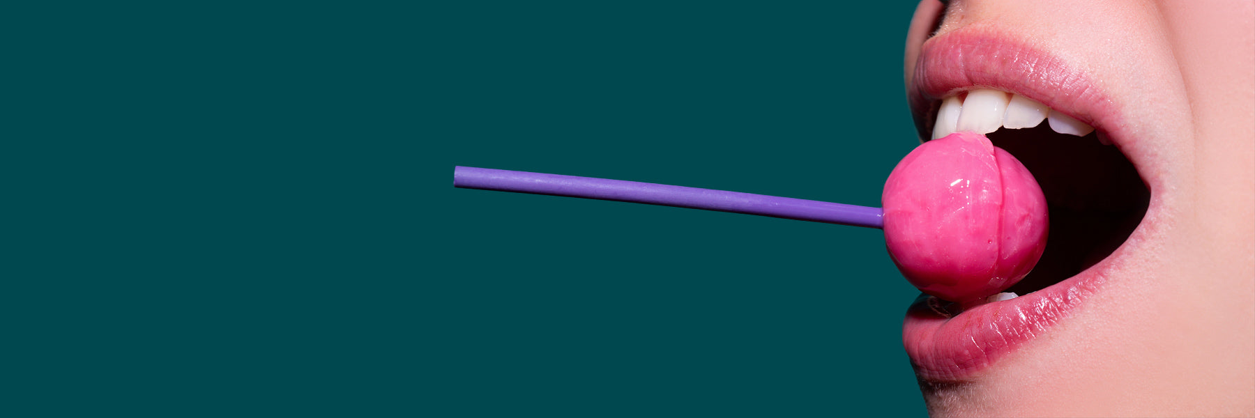 Close-up of a pink lollipop being sucked on against a teal background